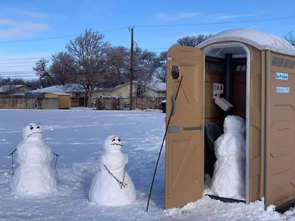 Schneemänner vor einer Toilettenkabine