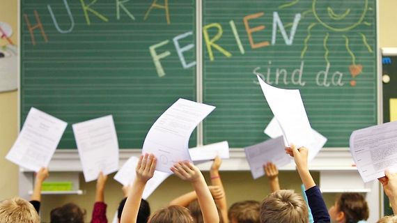 Kinder halten Papierbögen vor einer Tafel hoch