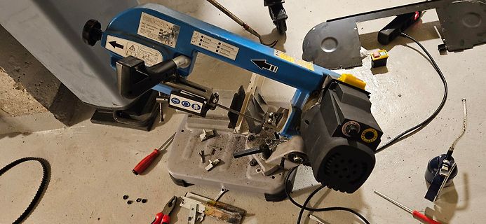 Blaue Bandsäge auf Werkstattboden mit Werkzeugen