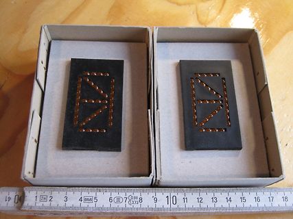 Zwei schwarze Bauteile in Kartons mit Maßband