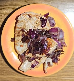 Gebratene Hähnchenbrust mit roten Zwiebeln auf orangefarbenem Teller