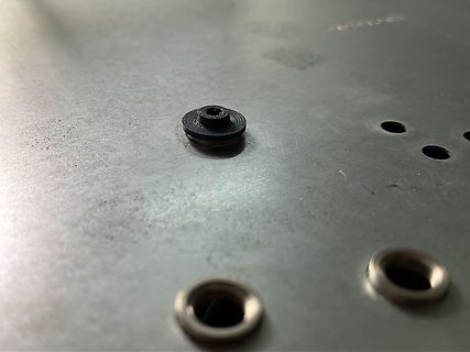 Nahaufnahme von Metalloberfläche mit Bohrungen und einem schwarzen Bauteil