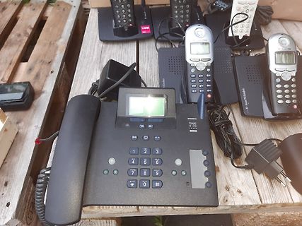 Diverse Schnurlose Telefone und ein Festnetztelefon auf Holzbrett