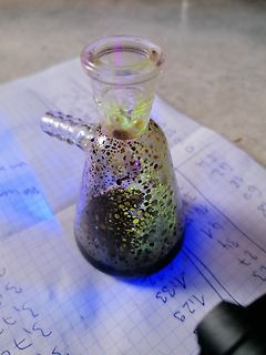Glasgefäß mit dunkler Flüssigkeit auf Papier