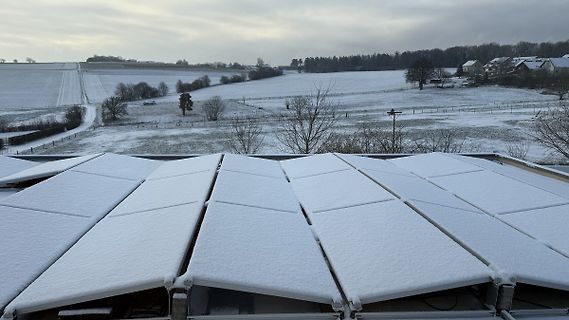 Schneebedeckte Solarpanels vor winterlicher Landschaft