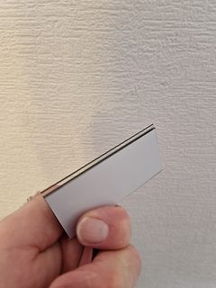Hand hält eine weiße Karte vor einer Wand