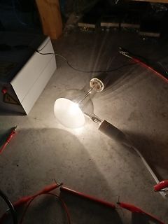 Leuchtende Glühbirne mit Krokodilklemmen und Netzgerät