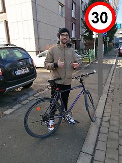 Mann mit Fahrrad vor Auto und Verkehrsschild