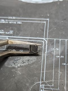 Bauteil mit Pinole in Pinzette auf Werkstattunterlage