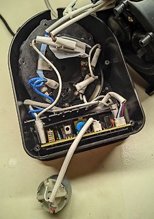 Innenansicht eines geöffneten Elektrogeräts mit Kabeln und Platine