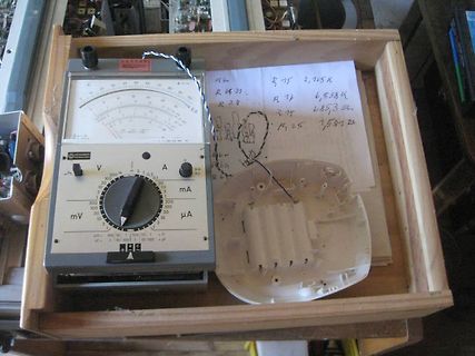 Analoges Multimeter und handgeschriebene Notizen auf Holzbrett