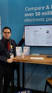 Mann an Messestand mit Laptop und Broschüren
