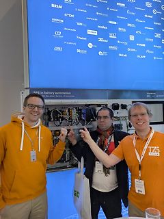 Drei Personen vor einem Display mit Firmenlogos