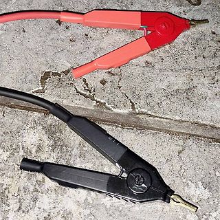 Rote und schwarze Krokodilklemmen auf Betonboden