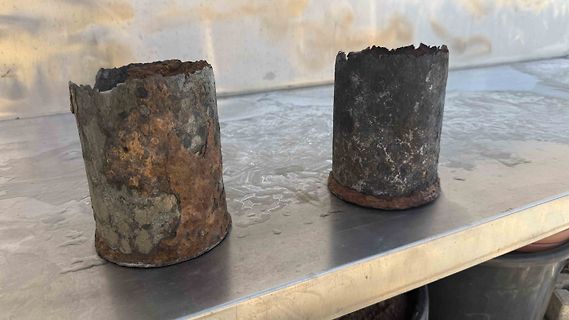 Zwei verrostete Metallzylinder auf Edelstahltisch