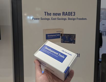 Hand hält Renesas Development Tools Box vor Werbeplakat