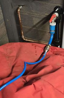 Wasserleitungen und blauer Schlauch an Holzwand