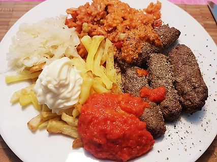 Teller mit Fleisch, Pommes, Sauerkraut und Saucen