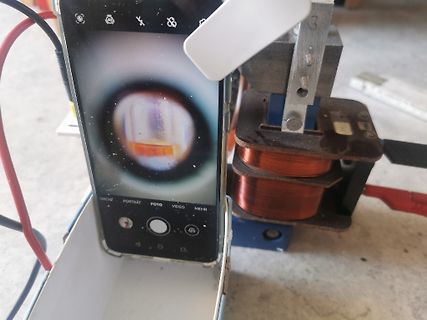Smartphone fotografiert Mikroskopbild neben Spule