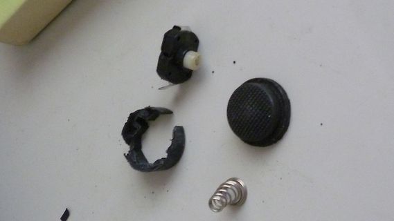Zerbrochene Teile eines Druckknopfs und eine Feder