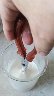 Hand hält Zange über Becher mit weißer Flüssigkeit