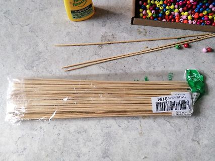 Holzstäbchen, Perlen und Kleber auf Tisch