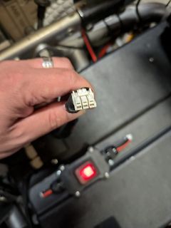 Hand hält elektrischen Stecker vor technischem Aufbau