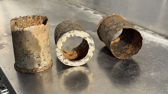 Drei verrostete Metallzylinder auf Edelstahltisch