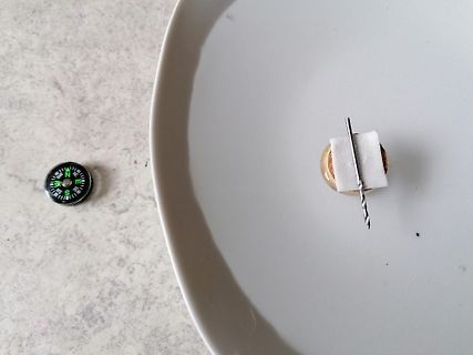 Kompass und Metallstab auf weißem Teller