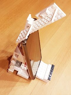 Smartphone in weißem Lego-Ständer auf Holztisch