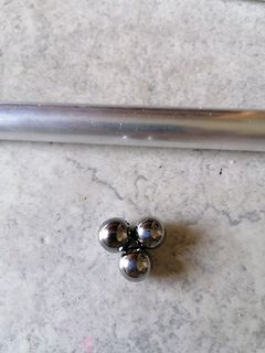 Drei Metallkugeln und ein Metallstab auf Steinboden