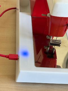 Rotes Gerät mit blau leuchtender LED und USB-Kabel