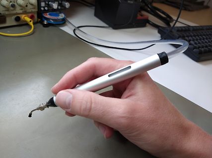Hand hält einen Lötkolben in einer Werkstatt