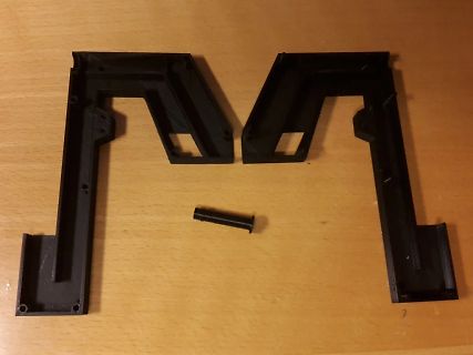 Zwei schwarze Kunststoffteile und ein kleiner Bolzen auf Holz