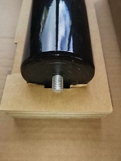 Schwarzer Zylinder mit Gewindebolzen auf Holzuntergrund