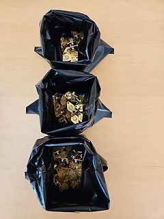 Drei schwarze Tüten mit goldenen Bauteilen auf Holz