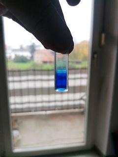 Hand hält Küvette mit blauer Flüssigkeit