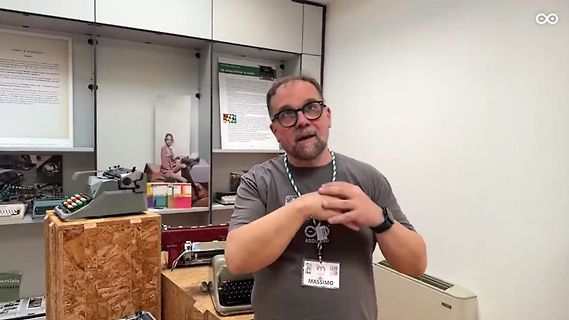 Mann mit Brille und Namensschild vor Schreibmaschinen