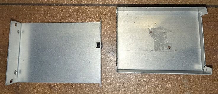 Zwei Metallgehäuse oder Blechabdeckungen auf Holzuntergrund