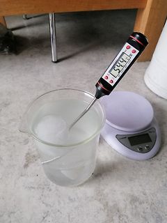 Digitalthermometer in Becherglas mit Flüssigkeit und Waage