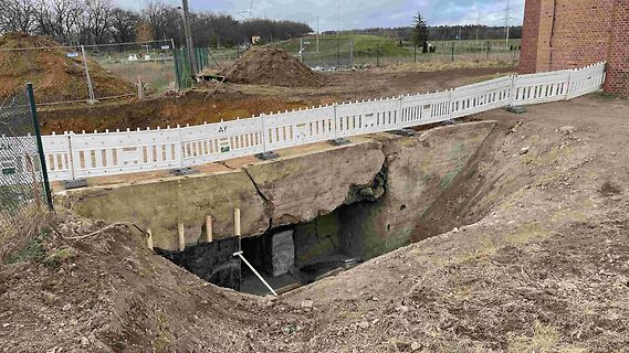 Baustelle mit Erdaushub und weißem Zaun