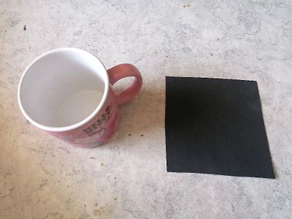 Rosa Tasse und schwarzes Quadrat auf Tisch
