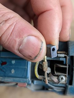 Hand hält ein kleines schwarzes Bauteil über einer Baugruppe
