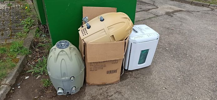 Entsorgte Elektrogeräte und Kunststoffbehälter im Freien