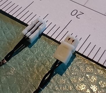 Zwei weiße JST-Stecker an Kabeln mit Lineal