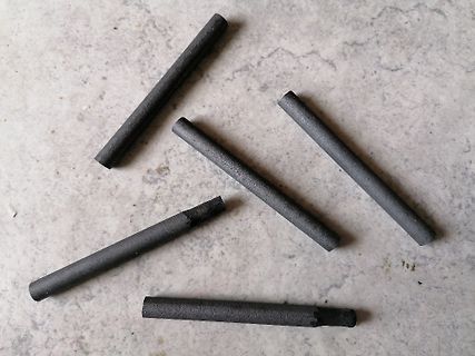 Fünf schwarze Kohlestäbe auf hellem Untergrund