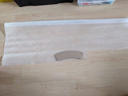 Weiße Textilunterlage mit braunem Pappauschnitt auf Holzboden