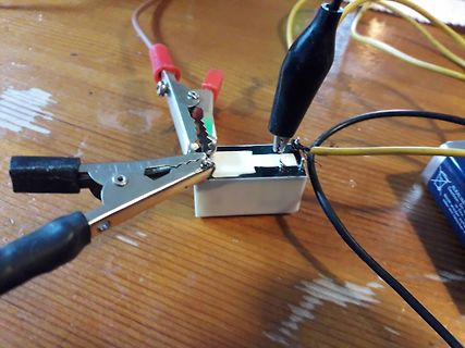 Aufbau mit Krokodilklemmen und Batterie auf Holztisch