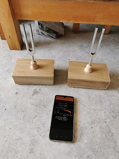 Zwei Stimmgabeln auf Holzsockeln und ein Smartphone mit Messwerten