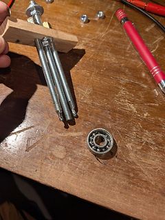 Mechanische Bauteile wie Gewindestangen und ein Kugellager auf Holztisch